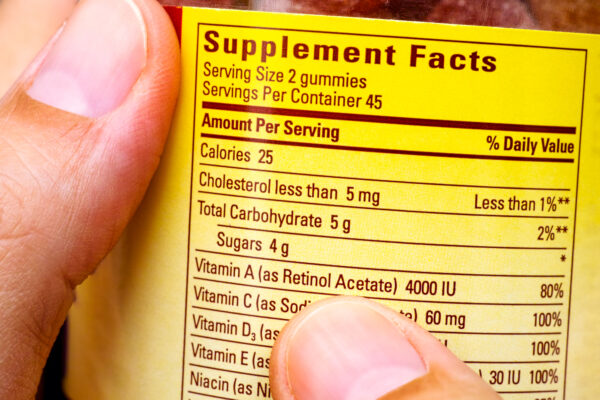 Plastic jar with supplement facts of multivitamins in woman hands. Close-up of Supplement facts of Dietary Supplement Bottle.