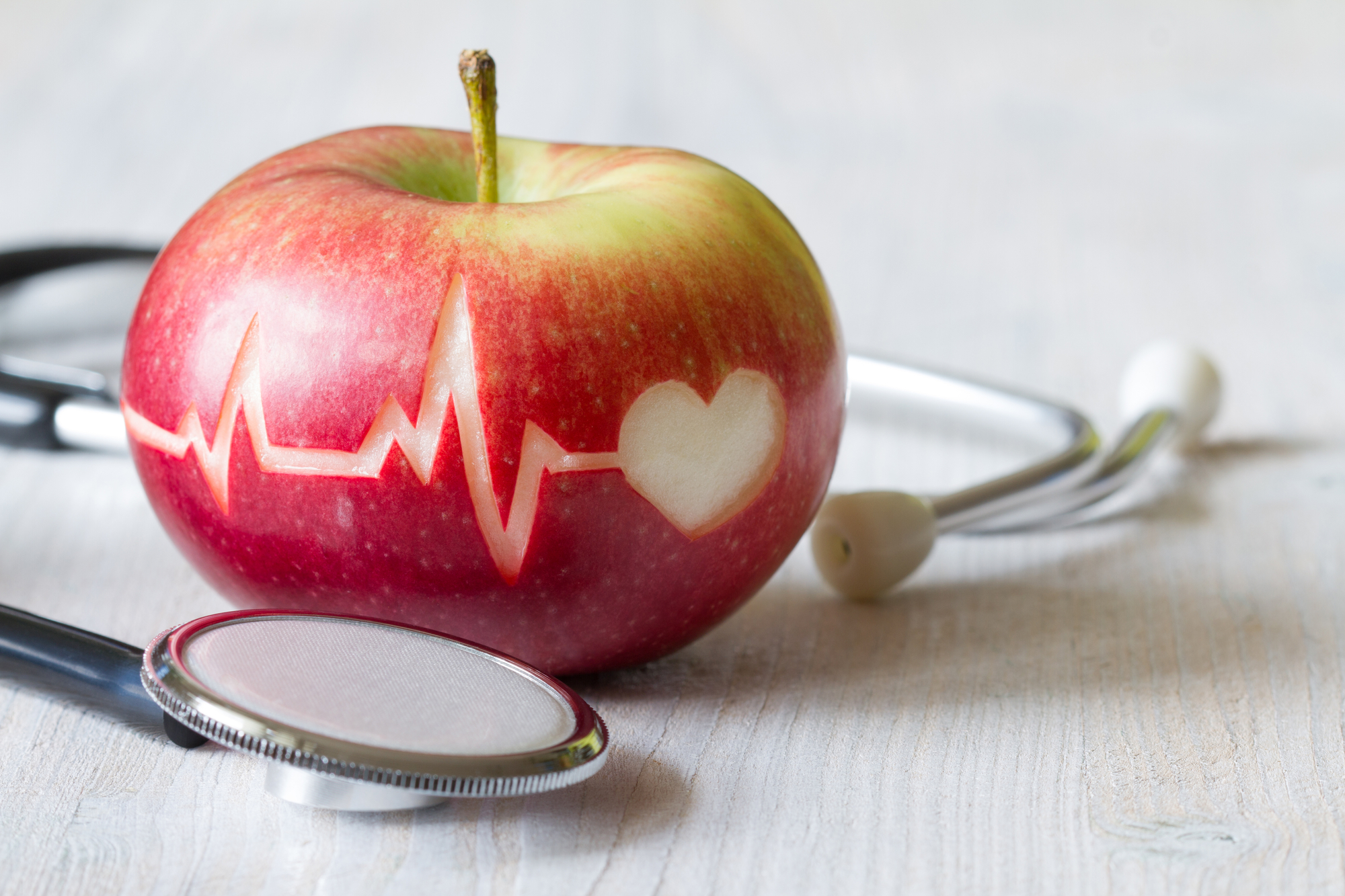 picture of apple and stethoscope on a table with ecg tracing etched in the apple